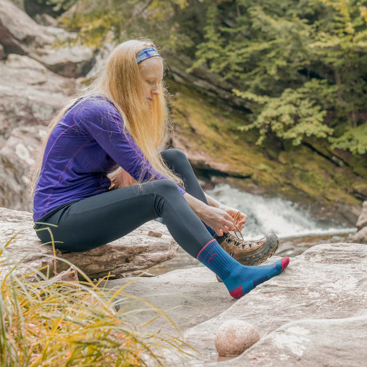 women sitting on rock putting on hiking shoes and wearing the 1903 micro crew hiking sock in midnight