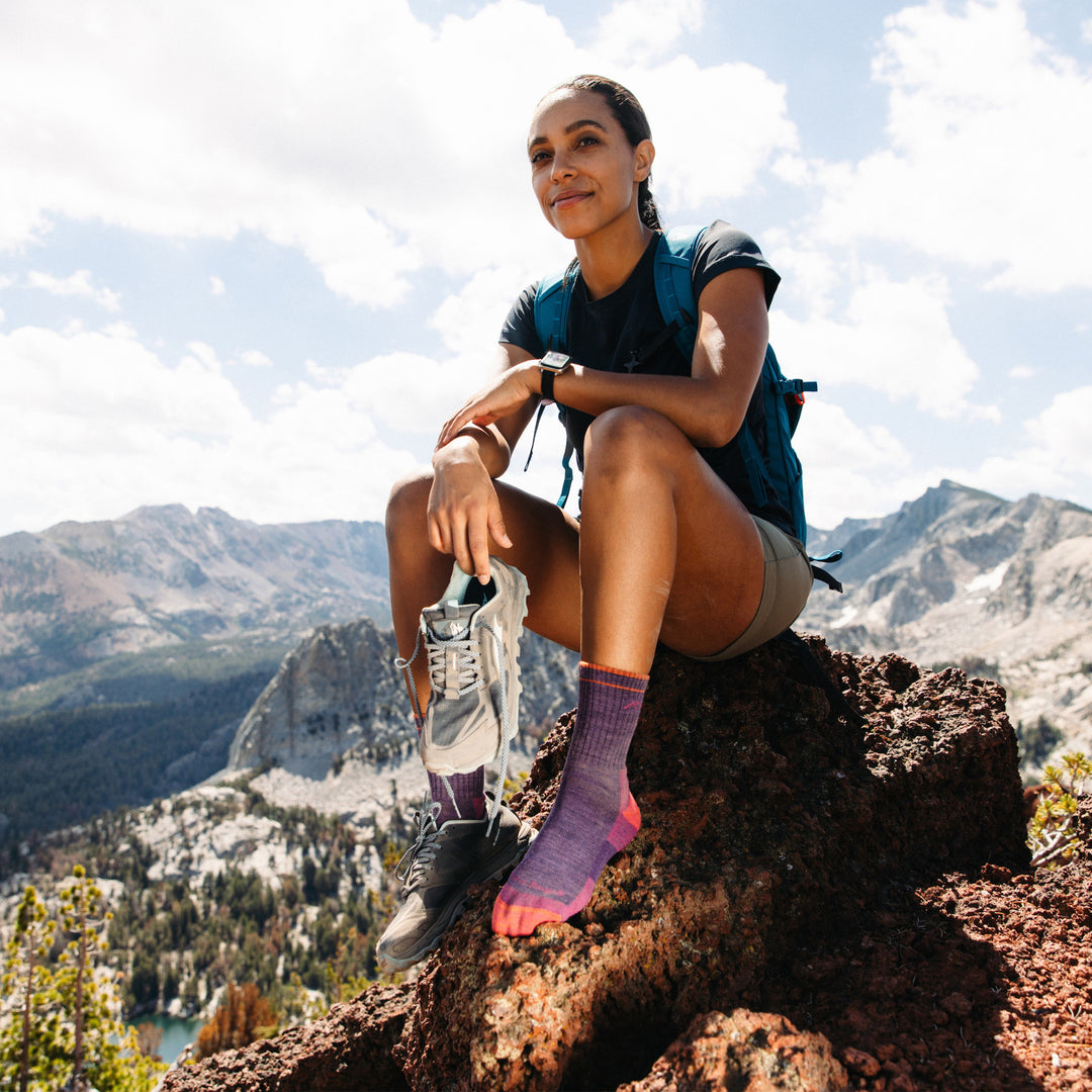 Model sitting on top of a mountain holding her shoe wearing the women's micro crew hiking sock in plum heather