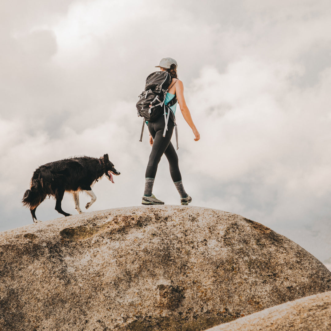 Woman hiking with her dog along a rocky ledge wearing Women's Hiker Boot Midweight Hiking Socks in Slate
