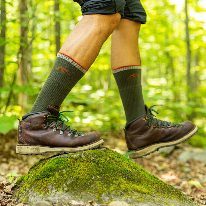 Man hiking in the forest, stepping over a rock wearing hiking boots and Coolmax Hiker Boot Hiking socks in gray/black