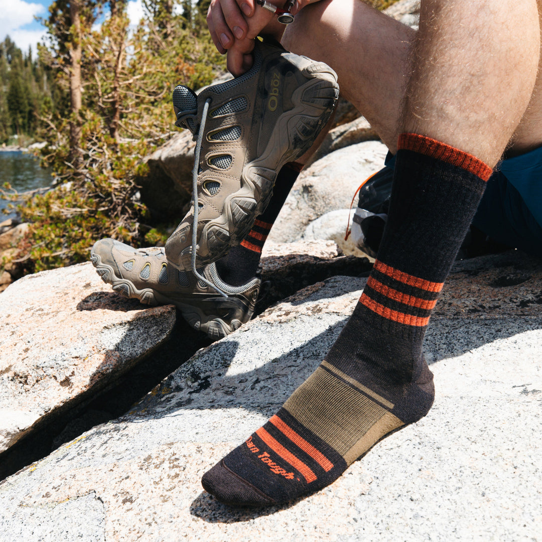 Close up shot of model sitting on the side of a mountain wearing the mens spur boot hiking sock in hickory