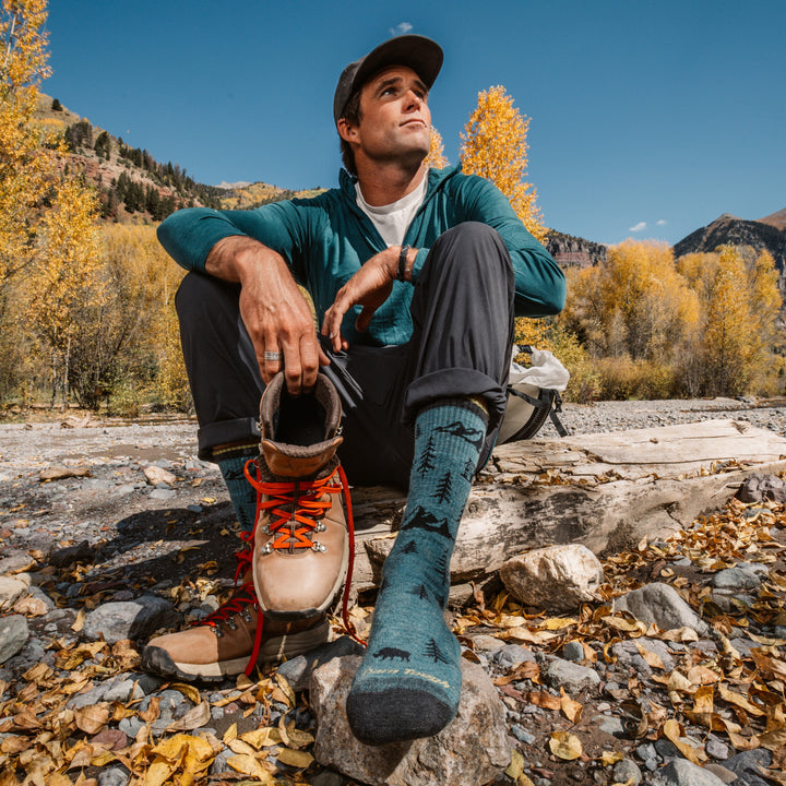 model sitting river side one shoe off showing the 1964 ABC boot sock in teal colorway