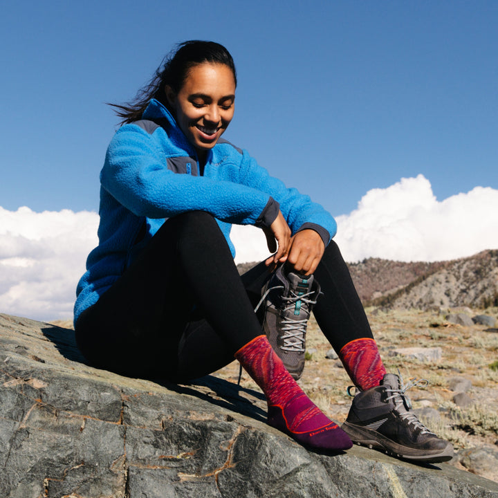 Model sitting on a rock putting on her hiking boots over the Women's Light Hiker Micro Crew Hiking Socks in Lunar Pink