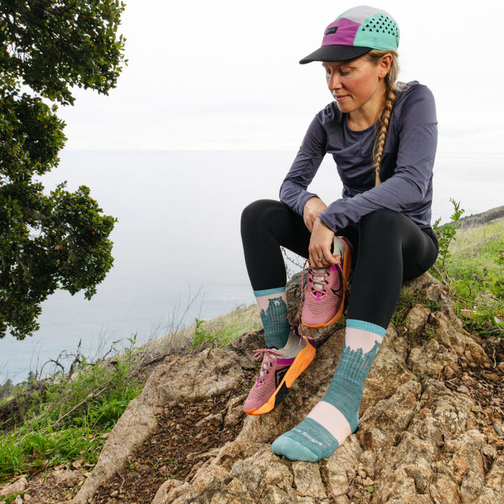 Model Sitting on rock atop mountain hold one shoe wearing the 1970 Beartown micro Crew Hiking sock in Quartz