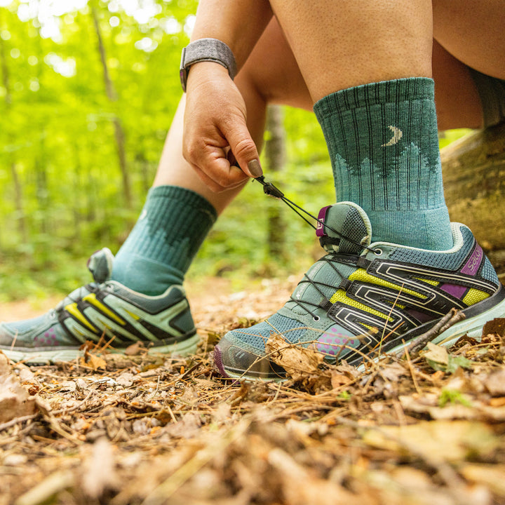 Close up shot of model sitting on a trail tying her shoes wearing the women's treeline micro crew hiking sock in aqua