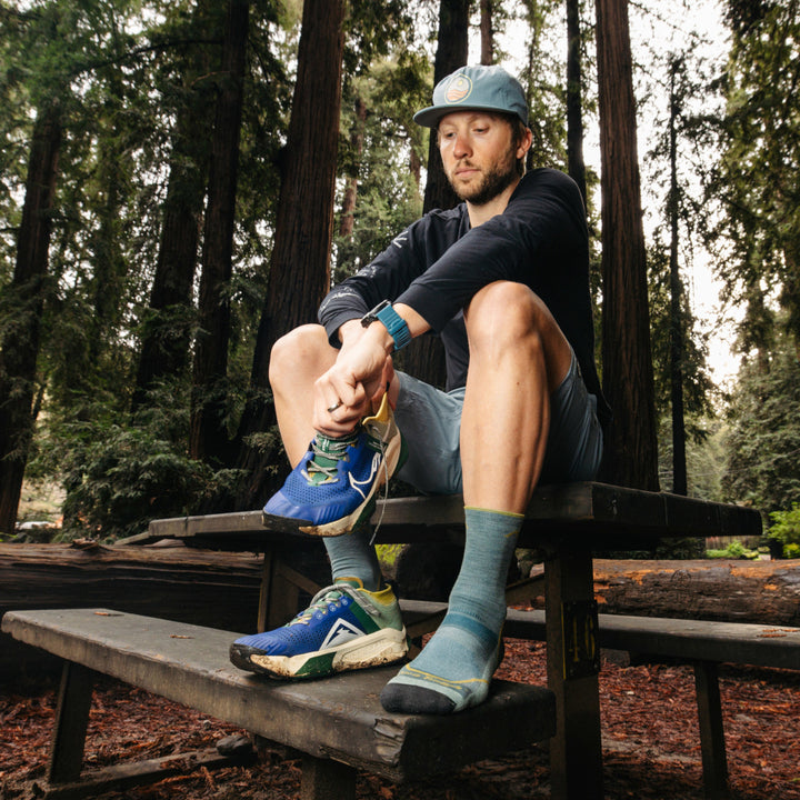 Model sitting on picnic table putting on sneaker wearing the 1972 Light Hiker Micro Crew hiking sock in Seafoam