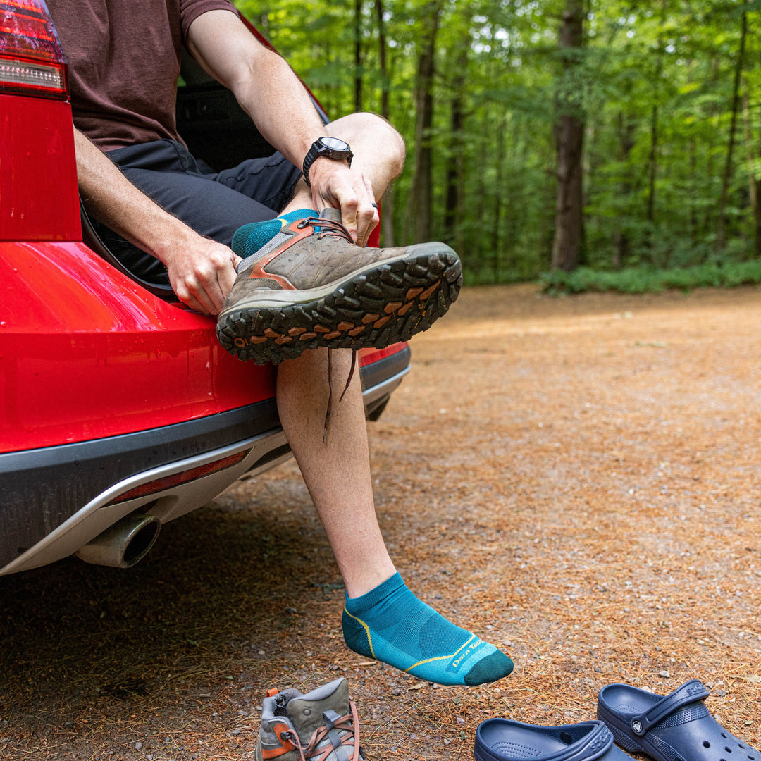 Model sitting in the trunk of a car putting on his shoes wearing the men's no show hiking sock in cascade
