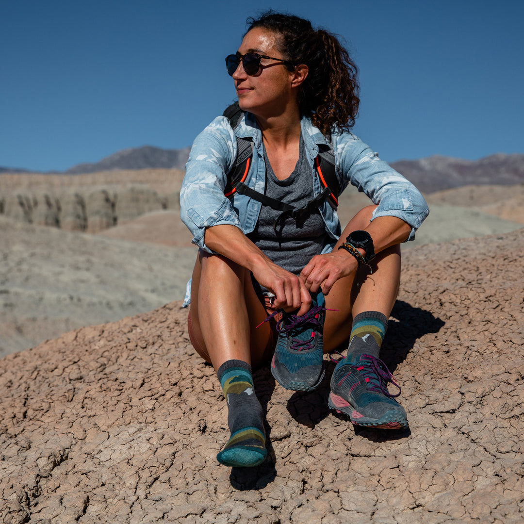 Model sitting down in nature wearing women's sunset ledge micro crew hiking sock in taupe while putting on shoes