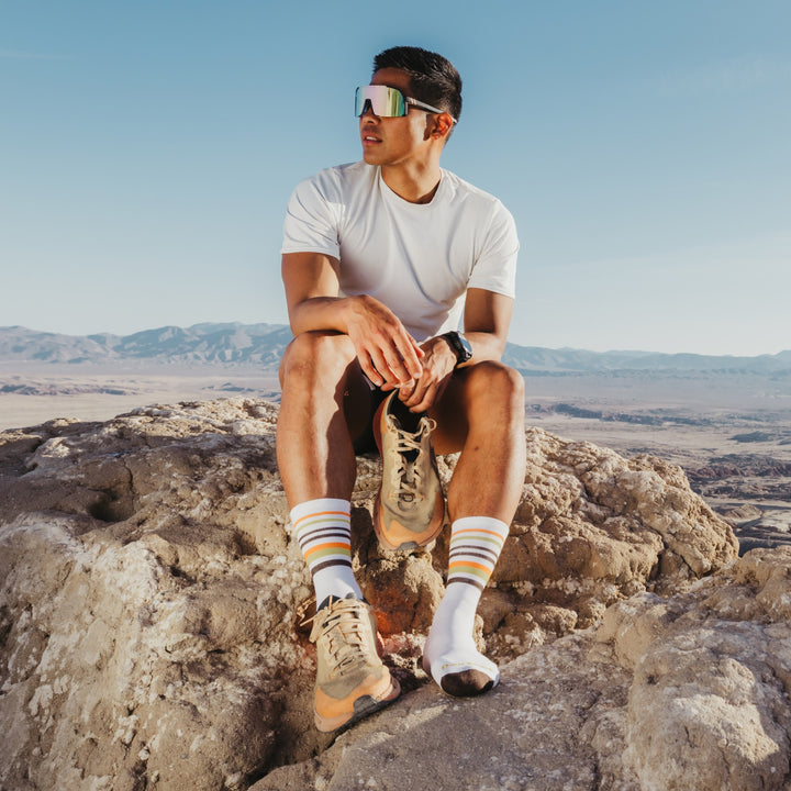 model sitting on the mountain top holding one shoe wearing the 5012 fast pack lightweight micro crew hiking sock in white colorway