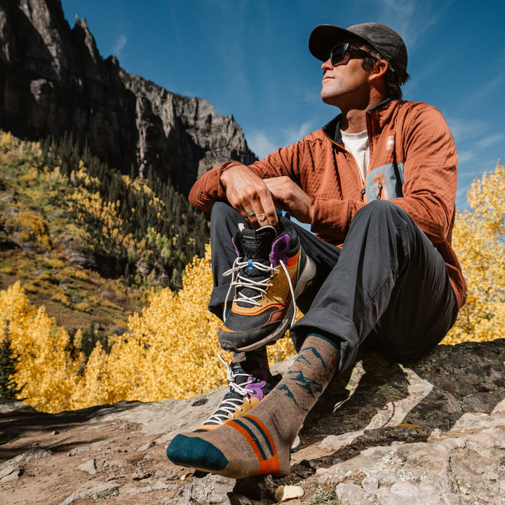 model sitting on rock with one shoe of showing the 5021 hut hut hike micro crew sock in bark colorway