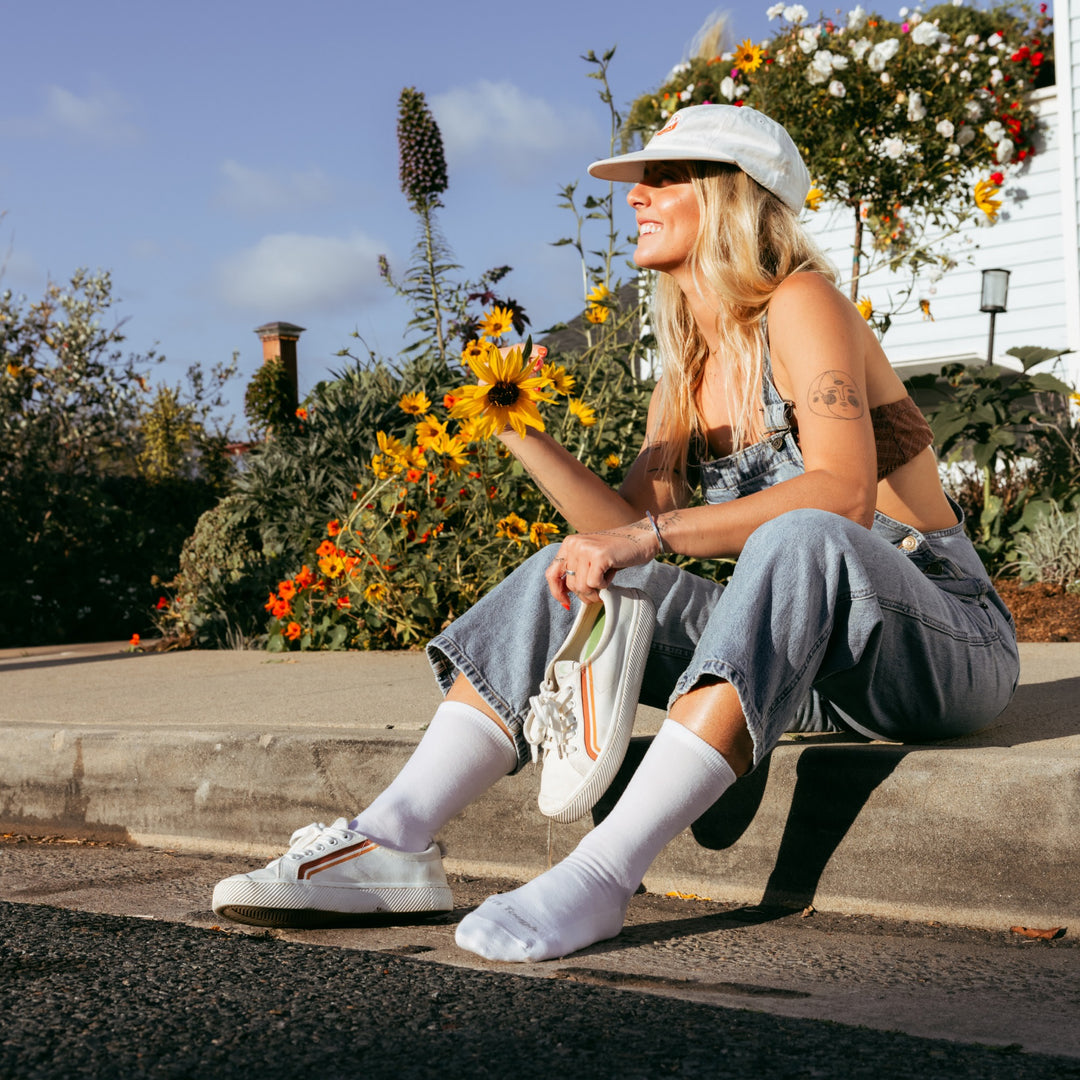 model sitting on the curb holding one shoe wearing the 6012 solid lightweight lifestyle crew sock in white colorway
