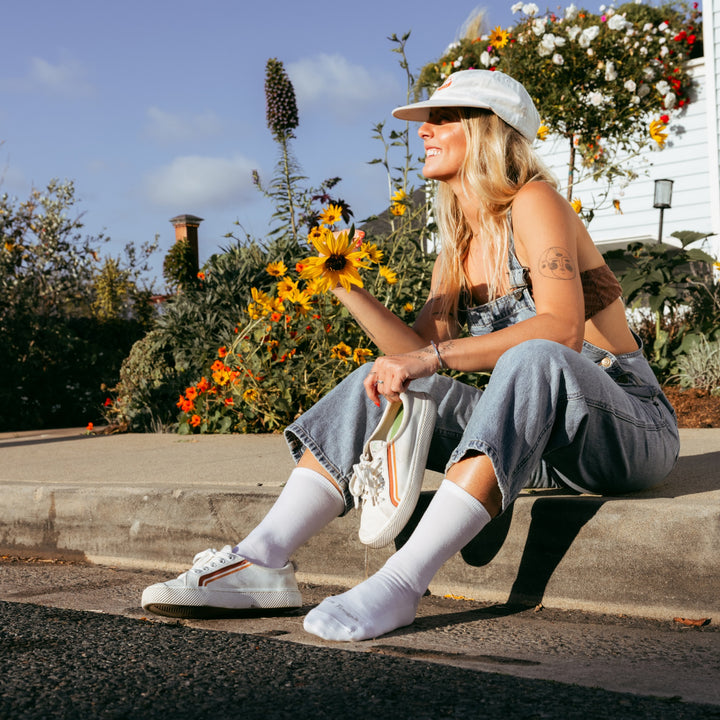 model sitting on the curb holding one shoe wearing the 6012 solid lightweight lifestyle crew sock in white colorway