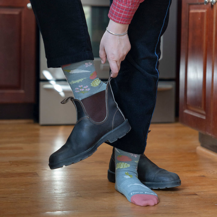 Model in a kitchen wearing women's farmer's market crew lifestyle sock in seafoam while putting on short boots