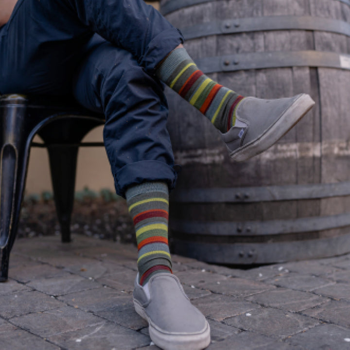 Model wearing rolled up blue pants and 6090 socks in cedar with gray sneakers sitting with legs crossed