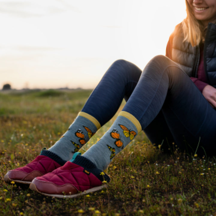 Model wearing purple slippers and 6109 socks in seafoam colorway sitting in a meadow at sunset