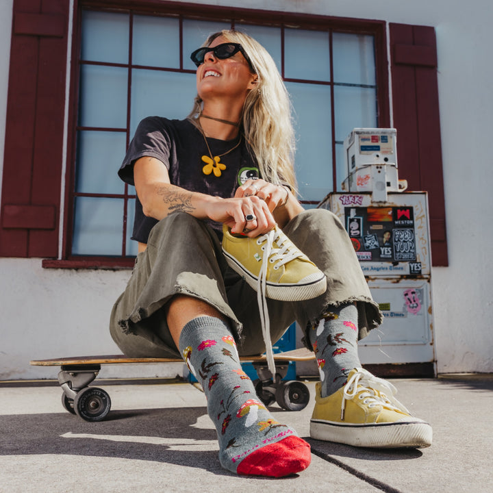 model sitting on a skateboard shoe in one hand wearing the shroom bloom lightweight lifestyle crew sock in seafoam colorway