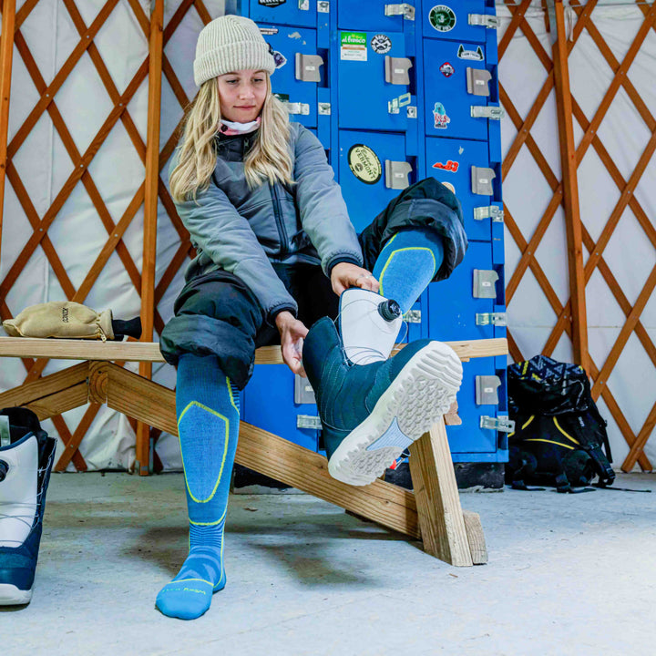Model putting on snowboard boot wearing the 8038 Outer Limits Ski and Snowboard sock in Cascade