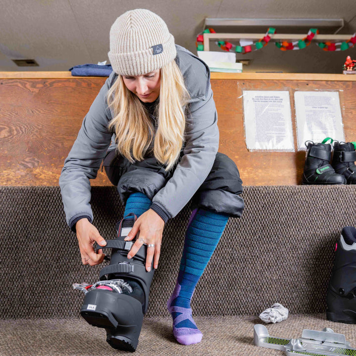 Model sitting in the lodge putting on ski boots wearing the  8040 Function X in eclipse