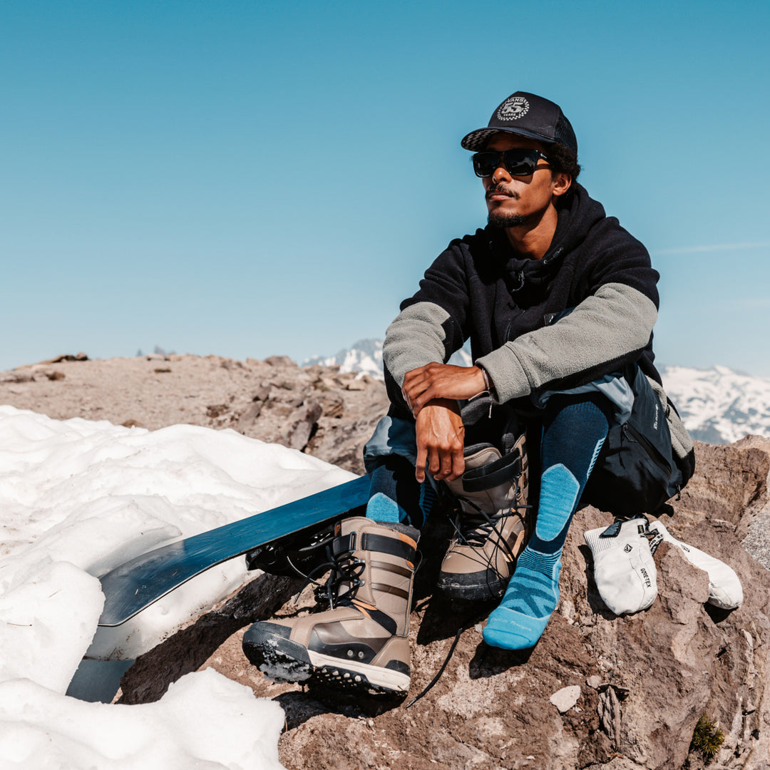 model sitting mountain top with one snowboard boot on and 8042 cobalt on other