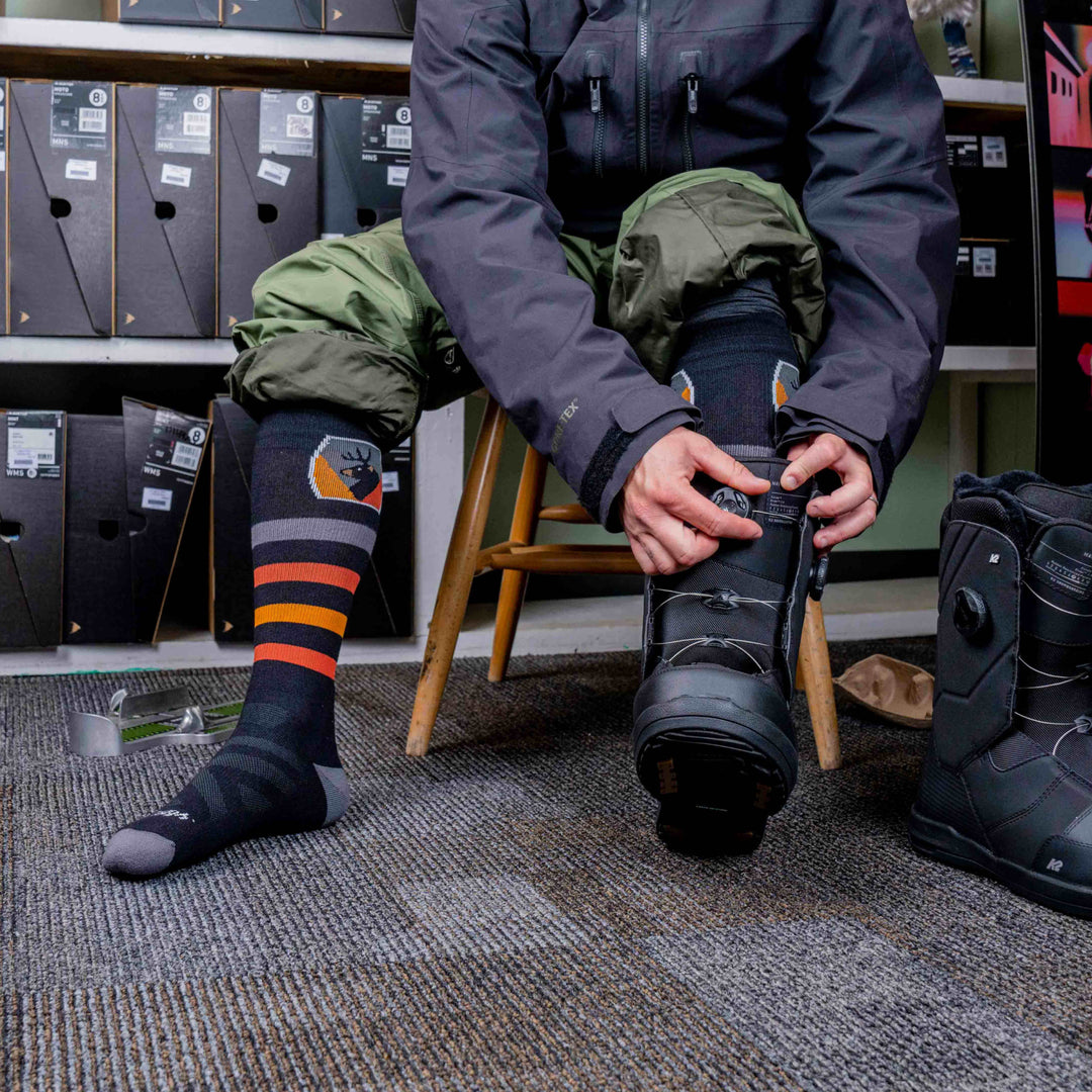 model sitting in chair putting on snowboard boots wearing the 8045 Thermolite over the calf beer badge in black