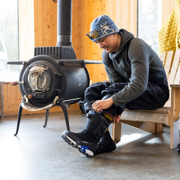 model sitting on chair next to woodstove putting on snowboard boot wearing 8061 carve OTC midweight with cushion sock black