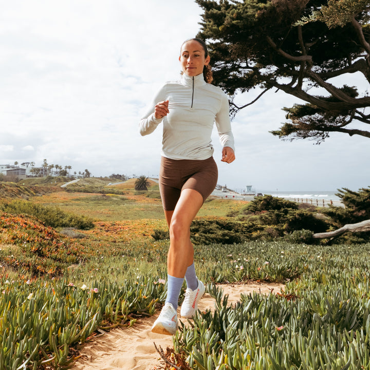 model running through field nest to ocean wearing the 1068 micro crew running sock in vapor blue colorway