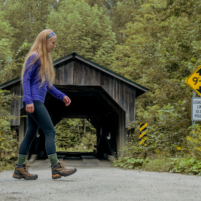Women walking past a covered bridge wearing hiking boots and the 1903 Limited edition color evergreen