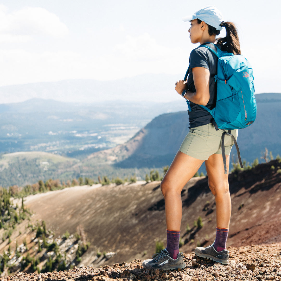 Woman standing looking out on the top of a mountain wearing the women's micro crew
 hiking sock in plum heather