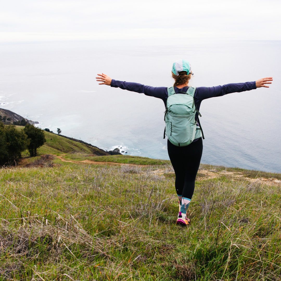 Model standing top of hill overlooking water wearing the 1970 Beartown Micro Crew hiking sock in Quartz