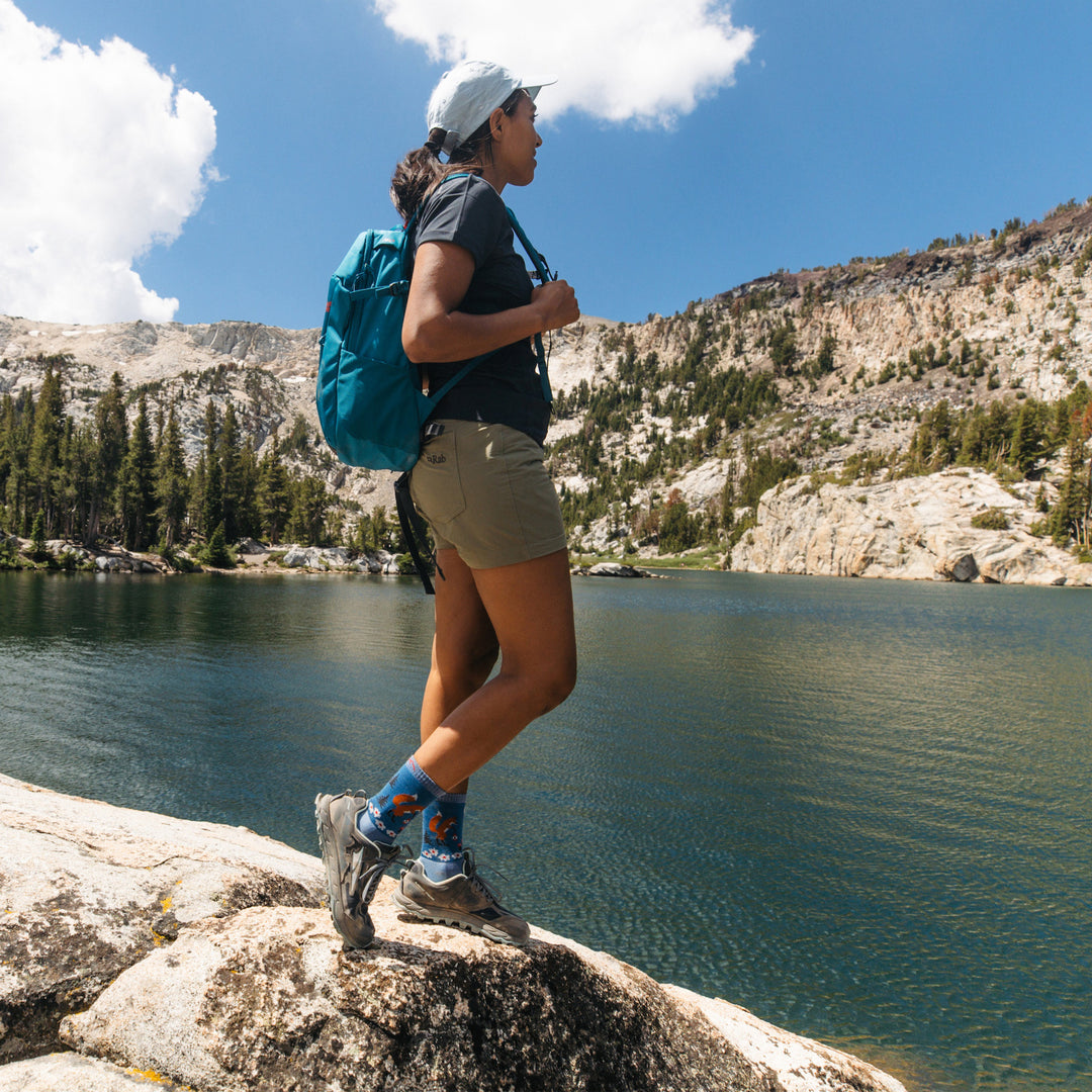 Full body shot of model standing next to lake wearing the women's critter club micro crew hiking sock in vapor blue