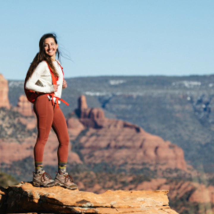 Model standing on rock against desert mountains and blue sky in background wearing 5016 socks in Taupe colorway