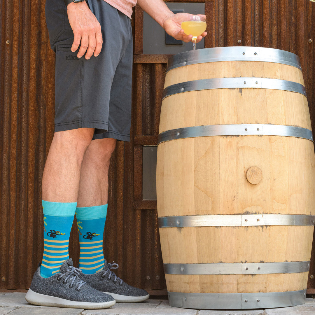 Shot of model standing next to a barrel with a drink wearing the men's wild life crew lifestyle socks in ocean blue
