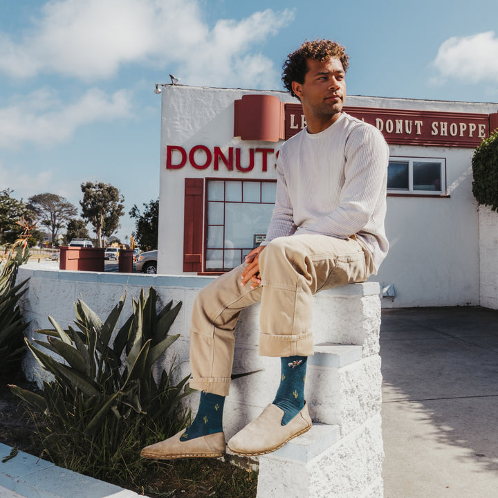 model sitting on wall wearing the wool'd wool'd west lightweight lifestyle crew sock in dark teal colorway