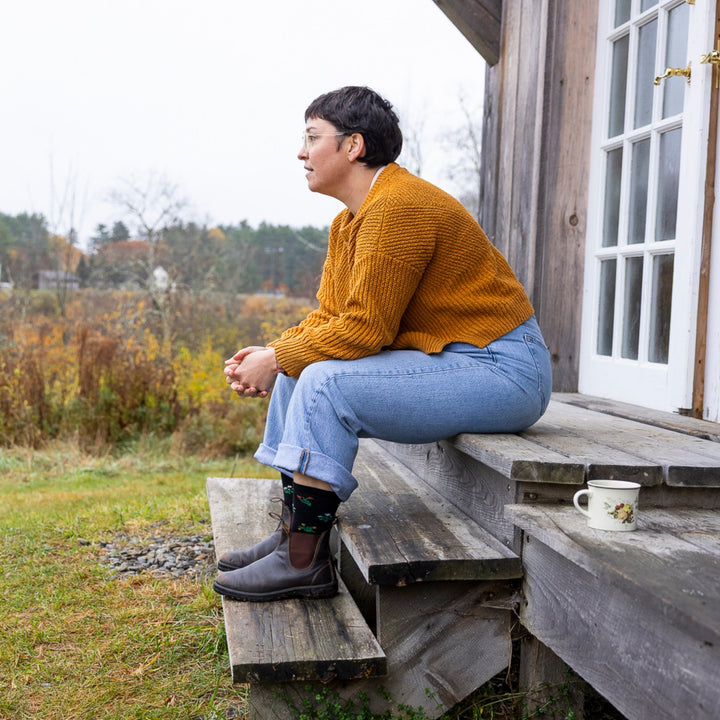 image of woman sitting on wooden stairs resting arms on legs wearing boots and 6139 wildflower crew lightweight with cushion black sock