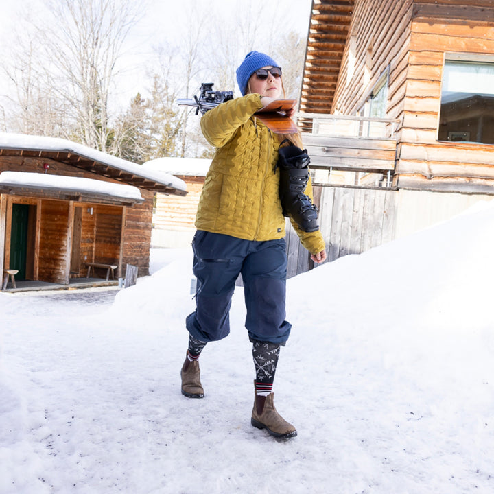 model carrying skis and ski boots with snowpants rolled up showing 8060 snowfall OTC midweight with cushion sock black