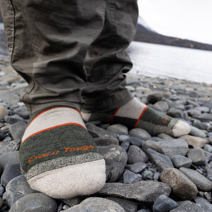 Close up shot of model standing on rocks by the lake wearing the men's full cushion boot hiking sock in olive