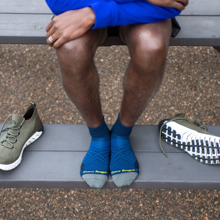 Close up of person on a picnic table, his feet on the bench with running shoes next to him wearing blue running socks