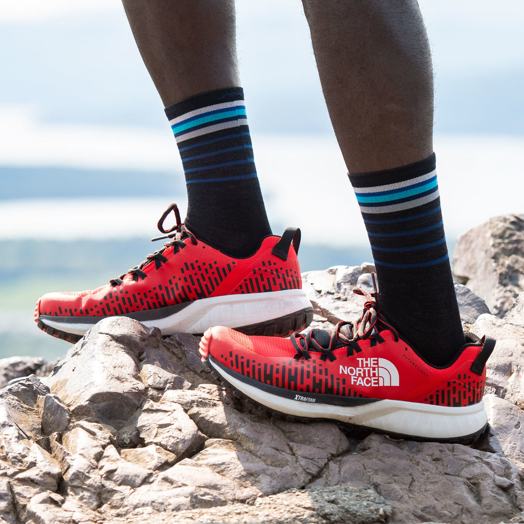 Man standing on a rock wearing red running shoes and Stride Micro Crew Ultra-Lightweight Running Socks in Black