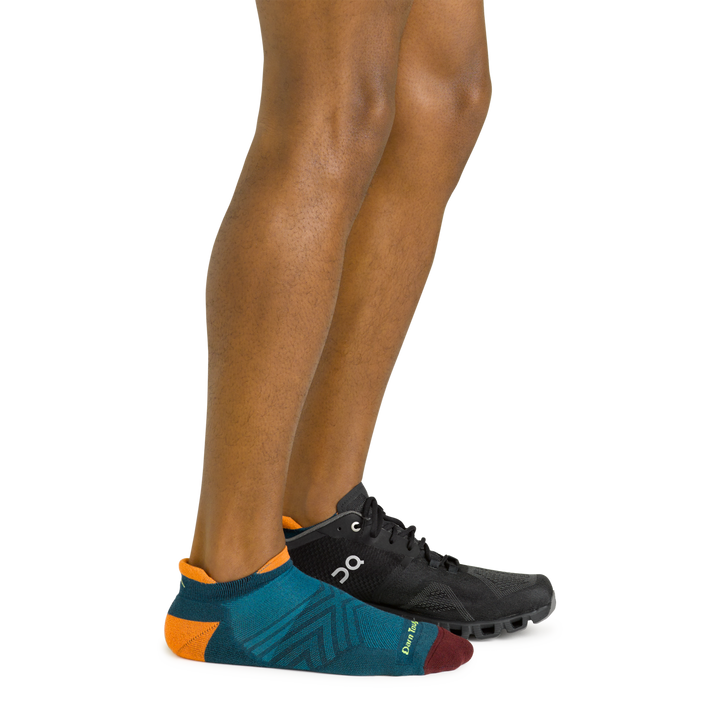 Side shot of model wearing the men's no show tab running sock in dark teal with a black sneaker on his left foot
