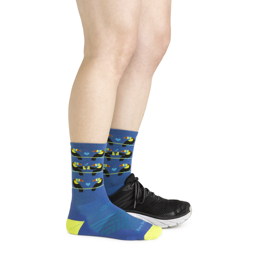 Model wearing the women's toco loco micro crew running sock in baltic blue with a black sneaker on her left foot