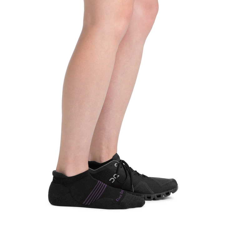 Side shot of model wearing the women's element no show tab running sock in black with a sneaker on her left foot