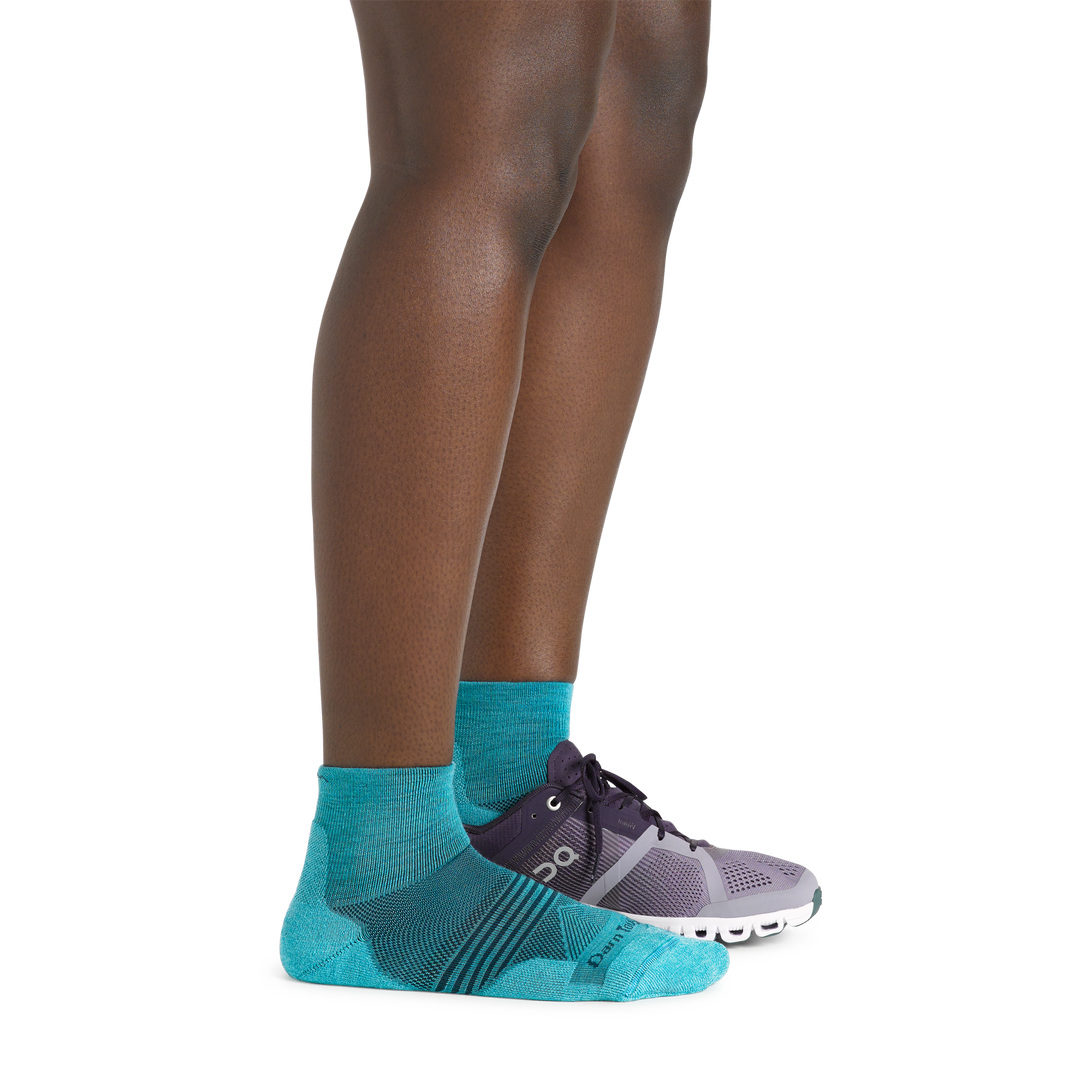 Side shot of model wearing the women's element quarter height running sock in cyan with a sneaker on her left foot
