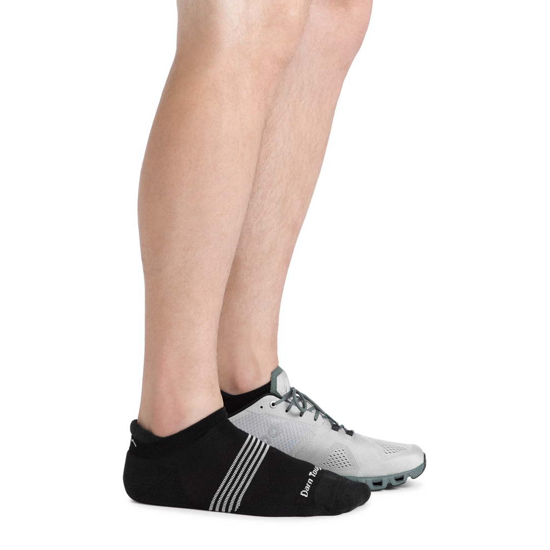 Side shot of model wearing the men's element no show tab running sock in Black with a gray sneaker on his left foot