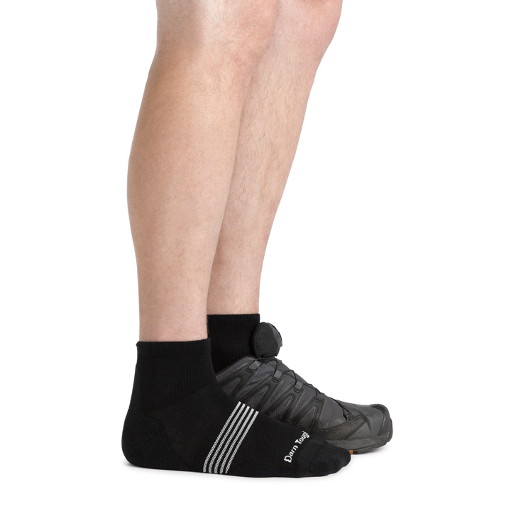 Side studio shot of model wearing men's element quarter running sock in black with gray sneaker on left foot