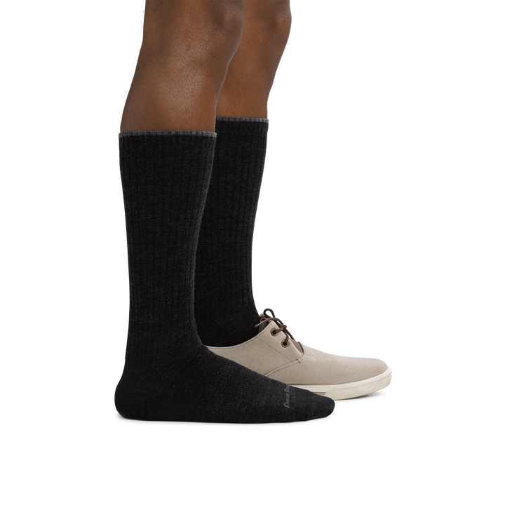 Man standing facing to the right wearing The Standard Mid-Calf Lightweight Lifestyle Sock in Black, with back foot in a shoe as well