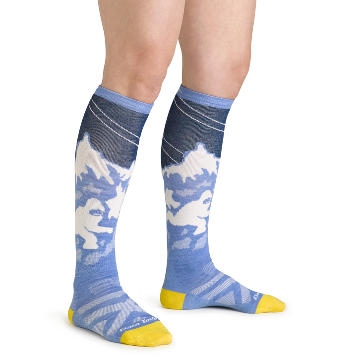 Close up studio shot of model wearing women's yeti over-the-calf midweight ski & snowboard sock in midnight blue