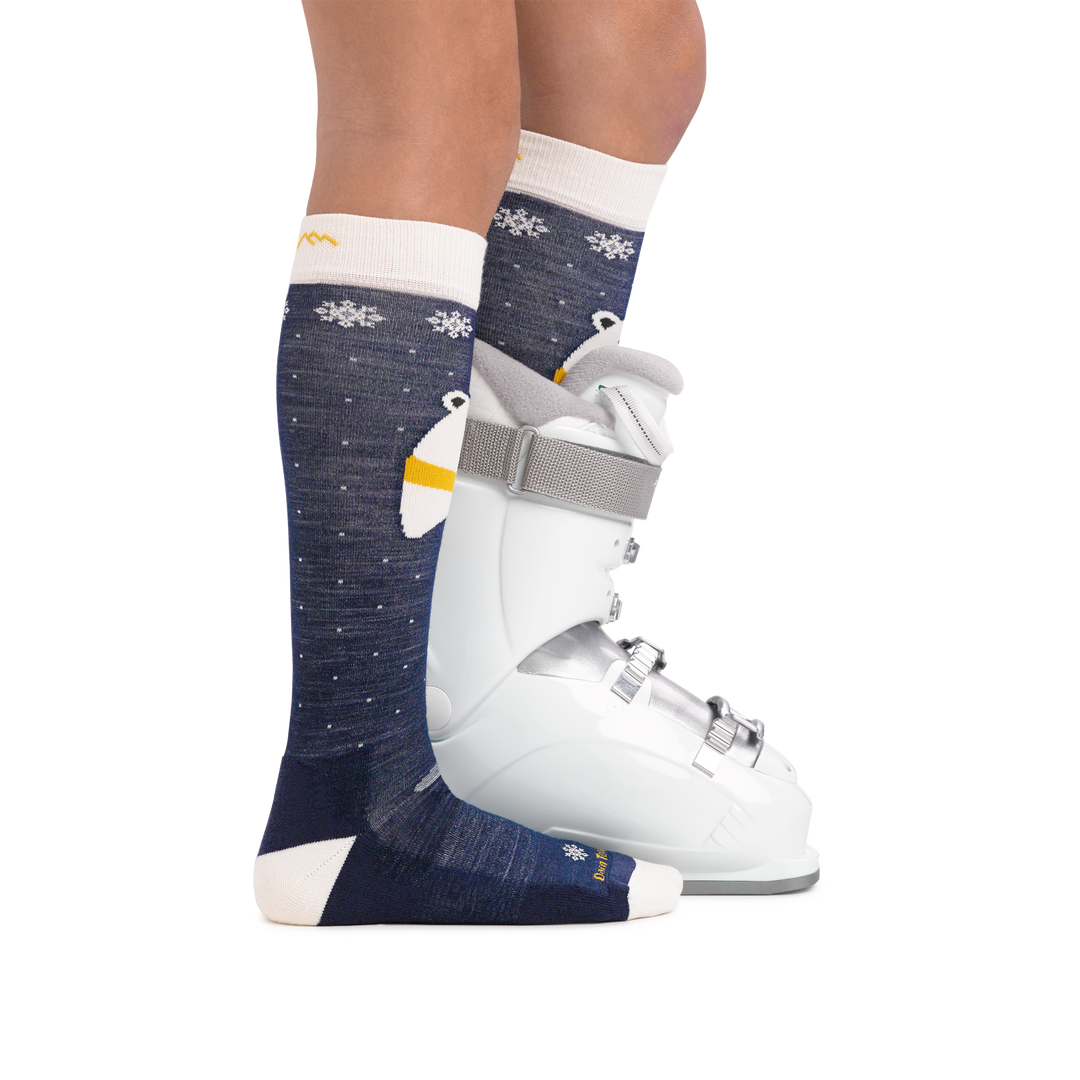 Kid wearing Kids Polar Bear Over the Calf Midweight Ski & Snowboard Sock in Blue with rear foot also in a ski boot