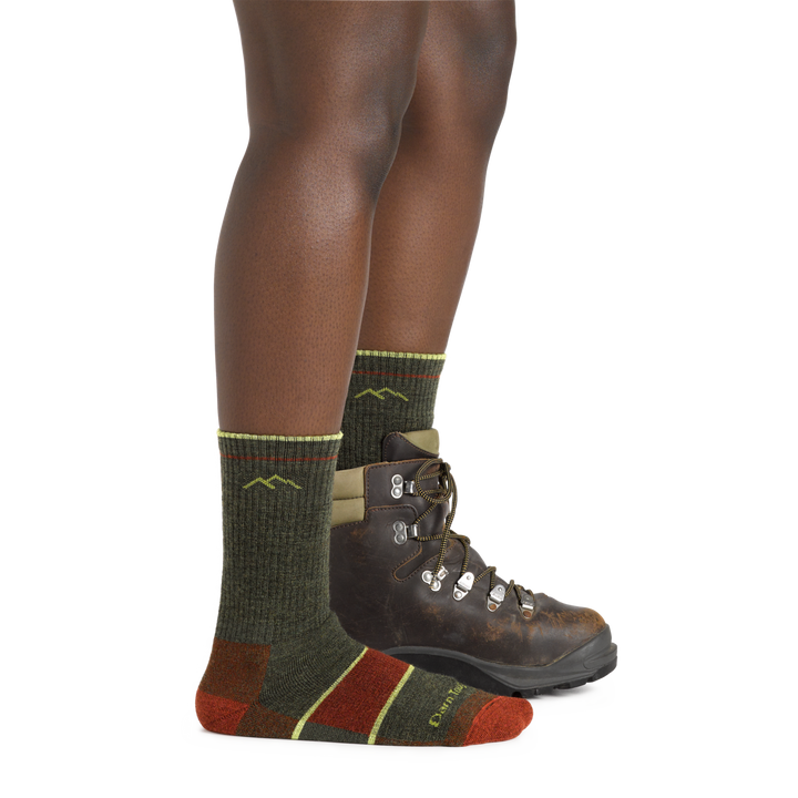 Studio shot of model wearing hiker boot socks in Forest and one brown boot, showing the sock's tall height.