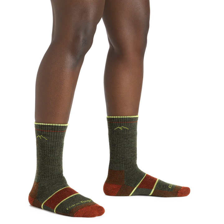 Studio shot of model wearing hiker boot socks in Forest. They are green with Yellow and orange accents.