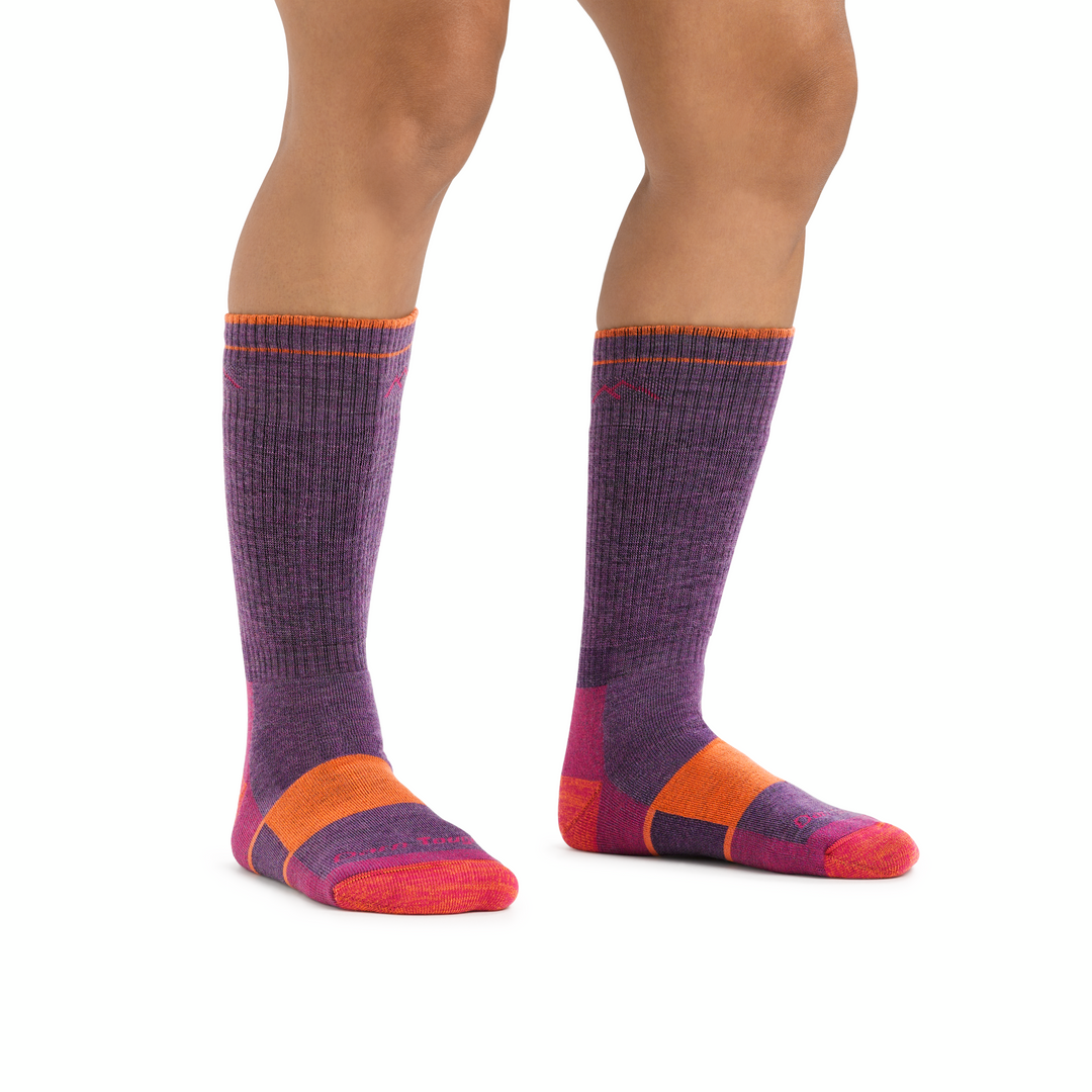 Studio shot of model wearing hiker boot socks in Plum Heather. They are purple with pink and orange accents.